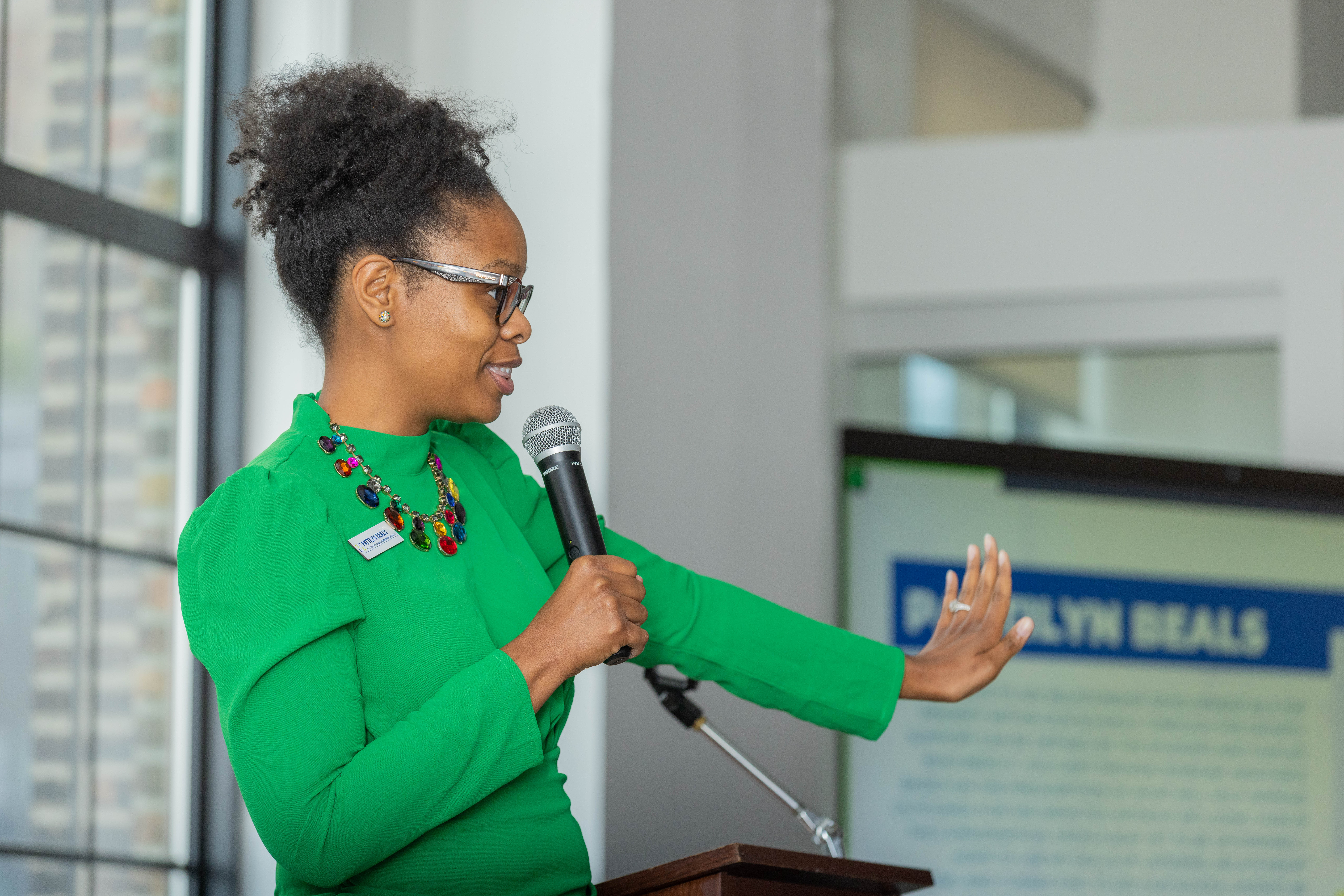 A speaker in a green outfit gestures while holding a microphone, discussing topics related to education and leadership.